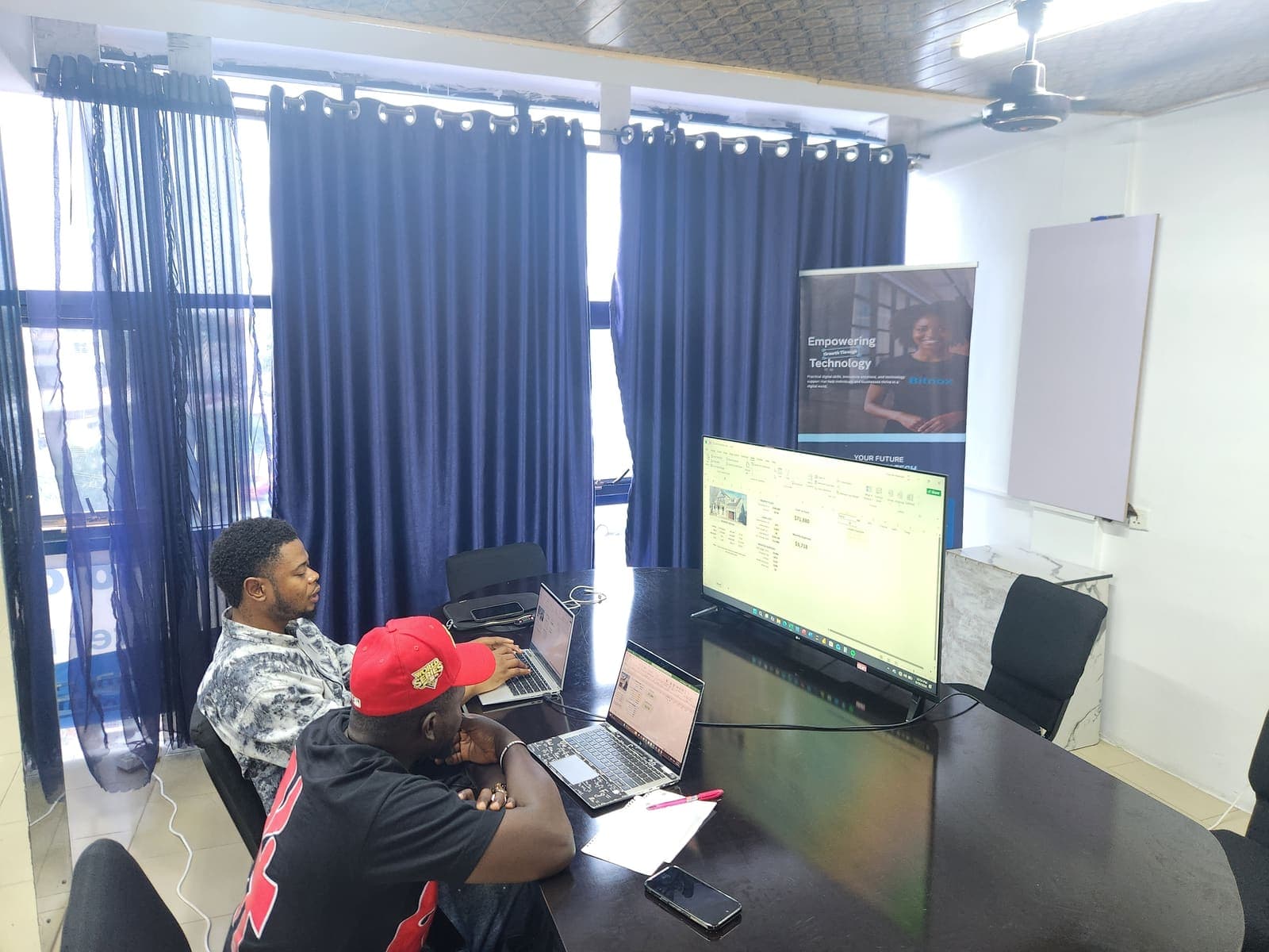 Two students working through a spreadsheet on their laptops in the Bitnox meeting room.