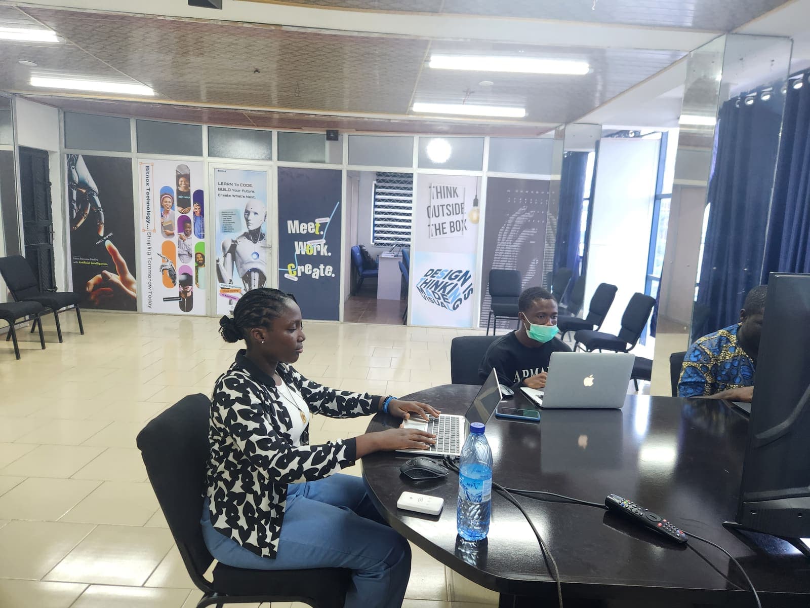 Learners at the open workspace beside the branded wall panels on the training floor.