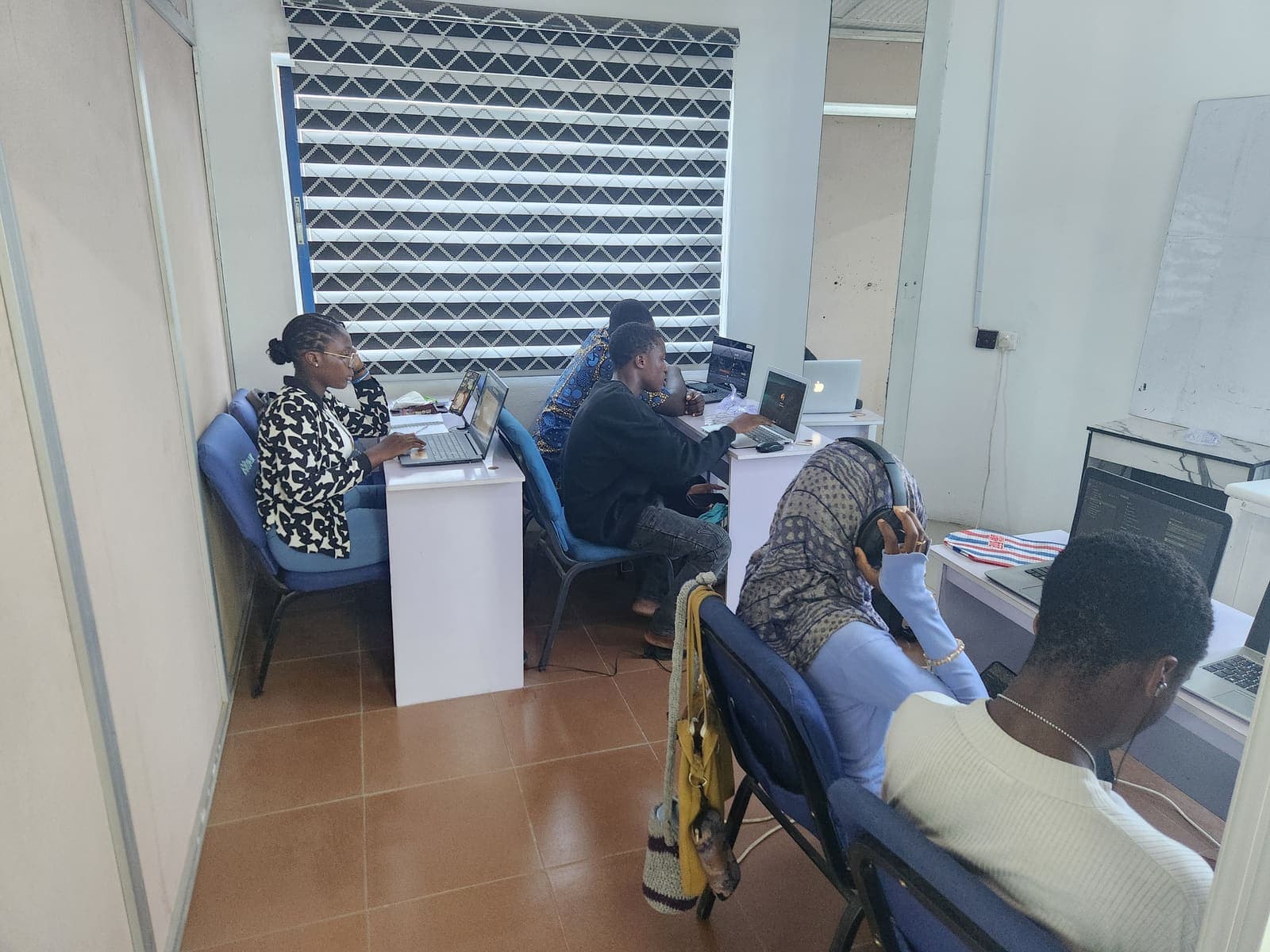 Students at work on their laptops in the lab room, one following a lesson in headphones.